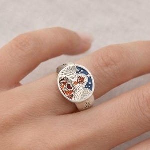 Puede incluir: Anillo de plata con un dise&ntilde;o de esmalte detallado y colorido. El anillo presenta una cara redonda con un tema celestial, que incluye una figura con cabello suelto, estrellas y un coraz&oacute;n. Los colores del esmalte son rojo, azul y blanco.