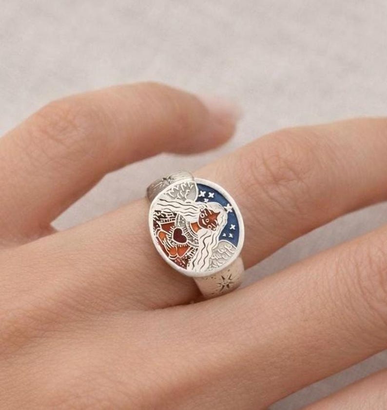 Puede incluir: Anillo de plata con un dise&ntilde;o de esmalte detallado y colorido. El anillo presenta una cara redonda con un tema celestial, que incluye una figura con cabello suelto, estrellas y un coraz&oacute;n. Los colores del esmalte son rojo, azul y blanco.