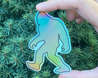May include: A holographic sticker of a Bigfoot walking, with a blue, green, and purple color gradient.