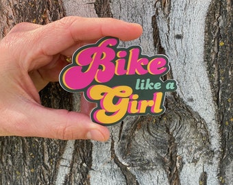 May include: A pink and yellow sticker with the text "Bike like a Girl" in a retro font.