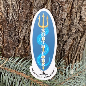 May include: Oval sticker with a blue background and a white outline. A gold trident with a blue wave design is in the center. The text "NORTH FORK PAYETTE RIVER, IDAHO" is written around the trident.