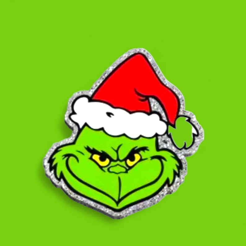 Pu&ograve; includere: Un adesivo sagomato glitterato raffigurante la testa di un personaggio verde dall'espressione accigliata e occhi gialli, che indossa un cappello da Babbo Natale rosso con bordo bianco. Il design &egrave; contornato da un bordo argento scintillante.