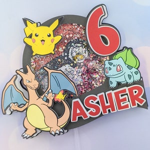 May include: A black and red cake topper with a Pokemon theme. It features a red number 6, a yellow Pikachu, a blue and orange Charizard, a green Bulbasaur, and the name Asher in red letters.