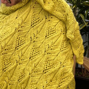 May include: A yellow knitted sweater with a geometric pattern. The sweater has a high neck and a loose fit.