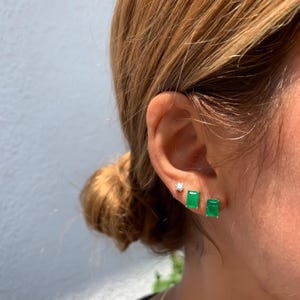 May include: A pair of emerald green rectangular earrings with a smaller diamond earring in the other ear.