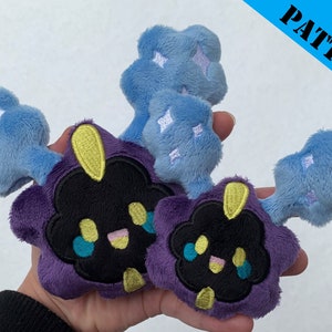 May include: Two plush toys of a dark purple and black cloud-like Pokemon with a yellow horn and blue tear-like markings. The Pokemon has a happy expression. The toys are holding blue fluffy clouds with white stars.