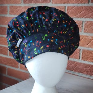 May include: A black chef's hat with a colorful musical note pattern. The notes are in shades of red, yellow, green, and blue. The hat is on a white mannequin head.