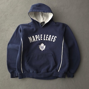 May include: A navy blue hooded sweatshirt featuring the white text MAPLE LEAFS arched across the chest. Below the text is a white Toronto Maple Leafs logo. The hoodie includes a white interior hood lining and white piping along the front sides.