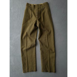 May include: Olive green high-waisted trousers featuring a button-fly closure, a structured waistband with visible button details, and pressed creases running down the centre of each leg. The trousers have a straight-leg silhouette and a textured fabric.