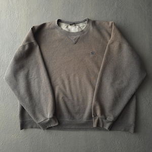 Peut inclure: Un sweat-shirt à manches longues et col rond de couleur gris anthracite délavé. Le vêtement présente un col côtelé avec un détail en V triangulaire sur le devant et un petit logo brodé sur la partie supérieure gauche de la poitrine.