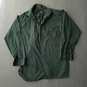 May include: A long-sleeved button-down shirt in a solid dark forest green colour. The shirt features a classic pointed collar, a single chest pocket on the left side, and buttoned cuffs. The fabric has a visible texture with subtle folds and creases.