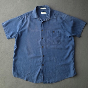 May include: A short-sleeved button-down shirt in a solid medium blue colour. The shirt features a standard collar, a single chest pocket on the left side, and dark brown buttons. A white label with the text ORVIS is visible at the inner neckline.