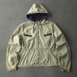 Peut inclure: Une veste à capuche beige clair dotée d'une fermeture éclair intégrale, d'une doublure de capuche bleu marine foncé et de deux poches de poitrine zippées horizontales avec bordure bleu marine. Manches longues à poignets boutonnés et taille cintrée.
