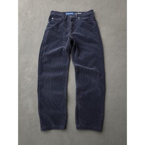 May include: Navy blue corduroy trousers with a relaxed fit. The trousers have a classic five-pocket design and a button and zip closure. The word "Relaxed" is visible on the waistband. The trousers are made of a soft, ribbed corduroy fabric.
