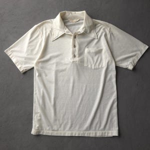 Peut inclure: Un polo à manches courtes blanc cassé doté d'un col pointu, d'une patte de boutonnage à trois boutons et d'une poche poitrine unique sur le côté gauche. Le vêtement est confectionné dans un tissu lisse et présente une étiquette intérieure.