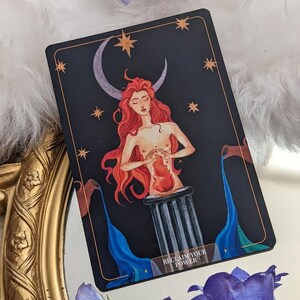 Puede incluir: Una carta de tarot con un fondo azul oscuro y una luna creciente. Una mujer con cabello rojo y un coraz&oacute;n rojo en sus manos se para sobre un pilar. El texto "Reclaim Your Power" est&aacute; en la parte inferior de la carta.