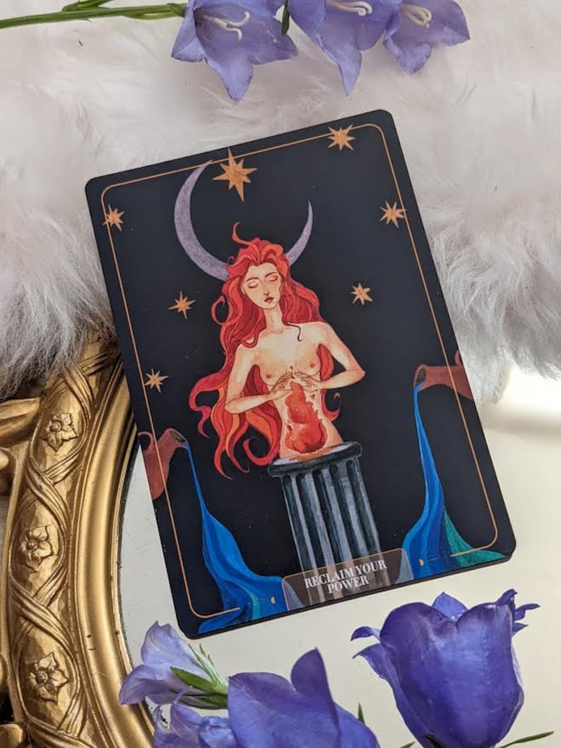 Puede incluir: Una carta de tarot con un fondo azul oscuro y una luna creciente. Una mujer con cabello rojo y un coraz&oacute;n rojo en sus manos se para sobre un pilar. El texto "Reclaim Your Power" est&aacute; en la parte inferior de la carta.