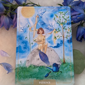 Puede incluir: Una ilustraci&oacute;n de acuarela de una mujer sentada en una roca con un limonero y p&aacute;jaros volando a su alrededor. La mujer sostiene un rollo que dice "Paciencia" en una escritura fluida. La imagen est&aacute; rodeada por un marco dorado y la palabra "Paciencia" est&aacute; escrita en la parte inferior.