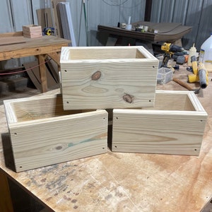 May include: Three unfinished wooden boxes stacked on top of each other. The boxes are made of light-colored wood and have a natural finish. The boxes are all the same size and shape.