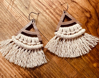 May include: A pair of wooden triangle earrings with a macrame fringe. The earrings are made of dark wood and have a natural, earthy look.