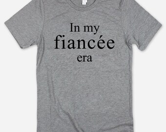 May include: Gray t-shirt with the text "In my fiancée era" printed in black.