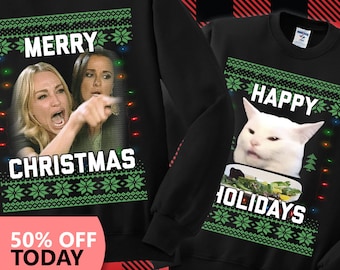 May include: Two black Christmas sweaters with a green and white snowflake pattern. One sweater features a woman yelling "Merry Christmas" and the other features a cat yelling "Happy Holidays".