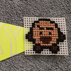 May include: A yellow triangular pennant with the word "SHOOOKY" written in white outlined letters. A small white square with a brown and black pixelated character is to the right of the pennant.