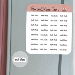 Puede incluir: Una hoja de pegatinas con el texto "Wash Sheets" repetido varias veces. Las pegatinas están sobre un fondo azul claro con un borde rosa. El texto "Fox and Rose Ink." está en la parte superior de la hoja.