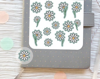 Puede incluir: Una hoja de pegatinas con margaritas blancas con centros amarillos sobre un fondo azul claro. Las pegatinas están etiquetadas como "Fox and Rose Ink." y "Daisy".