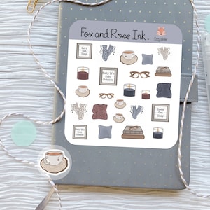 May include: A sheet of stickers with a fox and rose ink logo. The stickers feature illustrations of cozy winter themes, including mugs of hot drinks, candles, books, glasses, and knitted items. The text on the stickers reads "Let's Get Cozy" and "Baby It's Cold Outside".