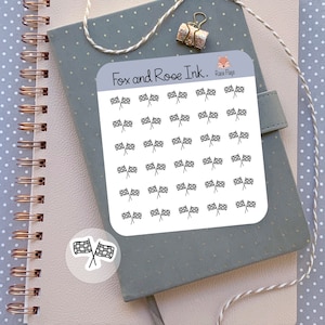 May include: A sheet of white sticker paper with black and white checkered flag stickers. The sheet has the text "Fox and Roe Ink." and "Race Flags" printed on it.