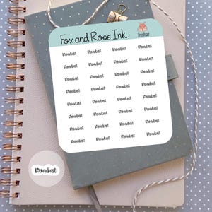 May include: A sticker sheet with the text "Broadcast" repeated multiple times, along with a smaller sticker of the same word. The stickers are on a light blue background, with the words in a handwritten style font. The sheet is on a notebook.