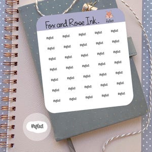 May include: A sticker sheet with the text "Perfect" repeated multiple times. The sticker sheet is white with rounded corners and the text is in a handwritten style. The sheet is on a gray notebook with a spiral binding.