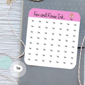 Op de afbeelding: Een vel roze stickers met het woord "Tap" herhaald. De stickers zijn van "Fox and Rose Ink." en hebben een vosillustratie. De stickers liggen op een grijs notitieboek.