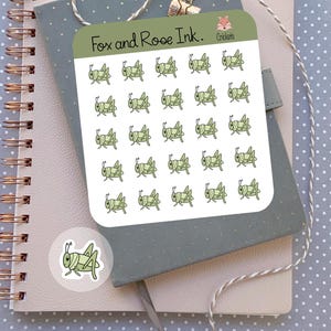 May include: A sheet of stickers featuring 36 green cartoon crickets. The stickers are arranged in a grid pattern on a white background. The sheet is labeled "Fox and Roe Ink." and "Crickets".