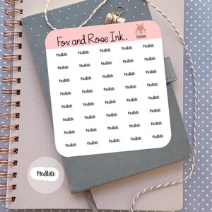 May include: A sheet of pink stickers with the word "Meditate" printed in black script. The stickers are arranged on a gray notebook with a spiral binding. The words "Fox and Rose Ink" are printed on the top of the sticker sheet.