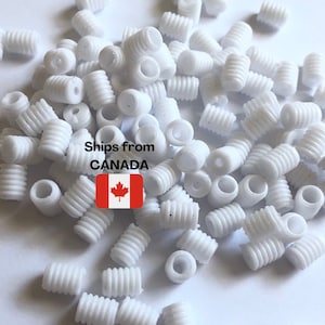 May include: A large pile of white plastic cord ends. The cord ends have a ribbed texture and a small hole in the centre. Ships from Canada.