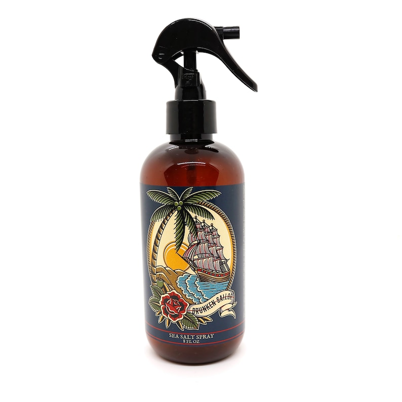 May include: A brown bottle with a black spray nozzle filled with sea salt spray. The bottle has a label with a nautical themed illustration of a ship sailing past a palm tree and a red rose. The label also includes the text "Drunken Sailor" and "Sea Salt Spray 8 fl oz".