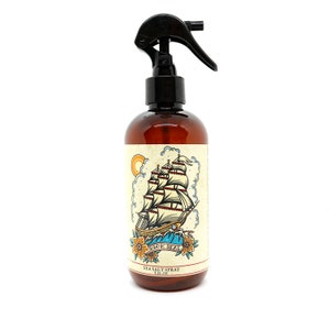 May include: A brown glass bottle with a black spray nozzle. The bottle has a label with a vintage illustration of a ship sailing on the high seas. The label reads "High Seas Sea Salt Spray 8 fl oz".