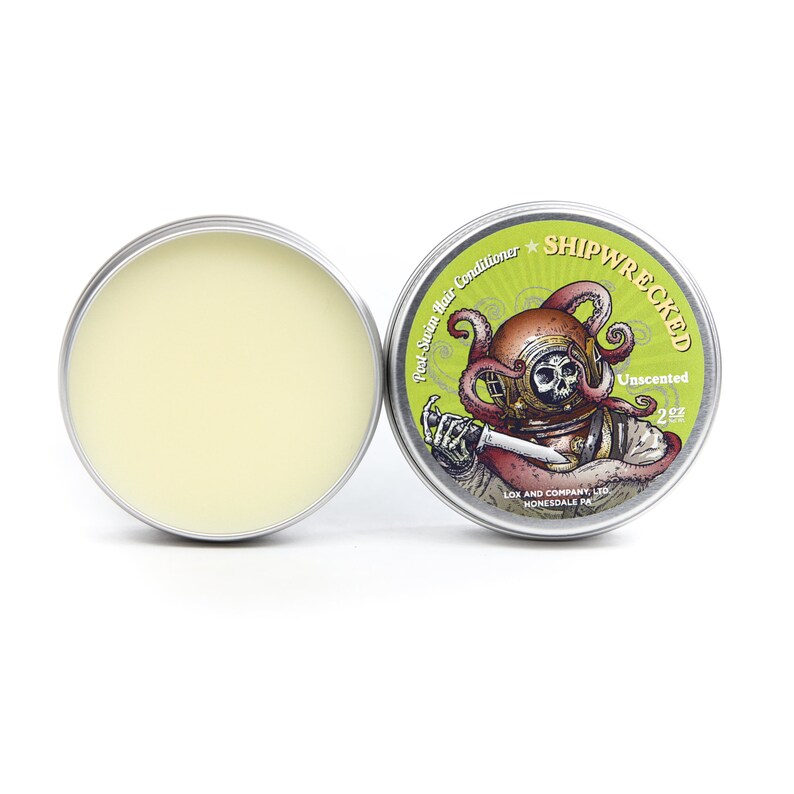 May include: A silver tin with a green and white label featuring a cartoon illustration of a scuba diver with an octopus wrapped around their head. The label reads "Post-Swim Hair Conditioner *SHIPWRECKED* Unscented 2 oz LOX AND COMPANY LTD HONESDALE PA".