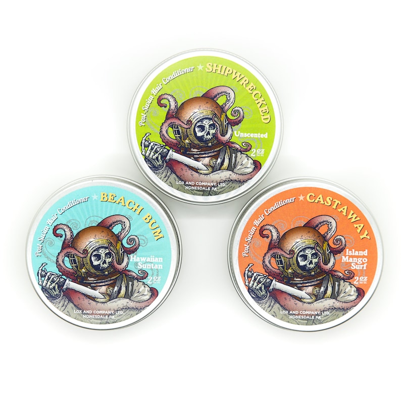 May include: Three round metal tins with colorful labels and illustrations of a scuba diver with an octopus. The labels read "Shipwrecked Unscented 2oz", "Beach Bum Hawaiian Suntan 2oz", and "Castaway Island Mango Surf 2oz".