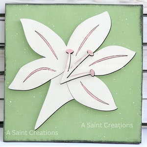 May include: A white wooden lily flower with pink accents on a green background. The flower is three-dimensional and has a layered look. The background has a speckled texture. The text "A Saint Creations" is printed at the bottom of the image.