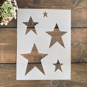 May include: A white stencil with four star shapes cut out. The stars are different sizes and are arranged in a random pattern.