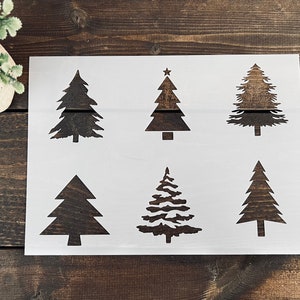 May include: A white stencil sheet with six different Christmas tree designs. The trees are all black and have a variety of shapes and sizes.