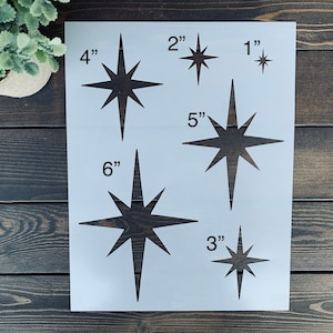 May include: A white stencil sheet with six different sized star shapes. The stars are all the same design, with eight points and a long, thin point at the top. The stencil sheet includes measurements for each star in inches: 1", 2", 3", 4", 5", and 6".