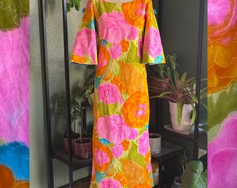 Könnte beinhalten: Ein Vintage-Kleid mit floralem Muster in Rosa, Orange und Grün. Es hat einen runden Ausschnitt und ausgestellte Ärmel. Der Stoff ist mit großen, stilisierten Blumen verziert. Das Kleid wird auf einer Schaufensterpuppe präsentiert.