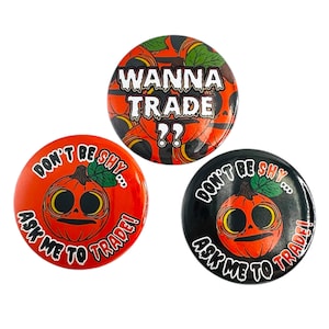 Puede incluir: Tres botones redondos con diseños de Halloween. Un botón tiene el texto "WANNA TRADE ??" sobre un fondo de calabazas. Los otros dos botones presentan una cara de calabaza y el texto "DON'T BE SHY... ASK ME TO TRADE!"