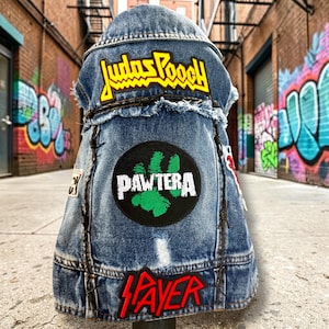 May include: A blue denim vest featuring a frayed collar and hem, decorated with three patches. The top patch reads Judas Pooch in yellow, the center patch shows a green paw print with the text Pawtera, and the bottom patch reads Slayer in red.