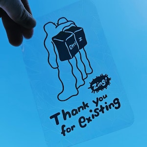 May include: A clear sticker featuring a black and white illustration of two figures carrying a computer keyboard key labelled "Ctrl Z". The sticker also includes the text "Thank You for Existing" and a small circle with the word "Zing!" inside.