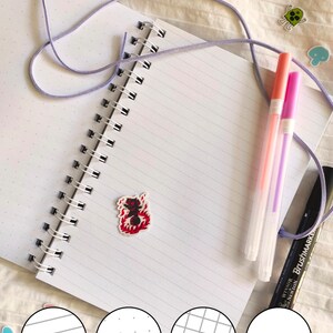 May include: Open notebook with spiral binding, featuring lined, dotted, graph, and blank pages. The text "Wonky lined, dotted, graph, blank pages are randomly placed" is visible. Includes pens and decorative stickers. The notebook has a variety of page styles.